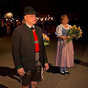 Der Obmann bei seiner Begrüßung, im Hintergrund einige der Tänzerinnen in Tracht mit Blumensträußen im Arm