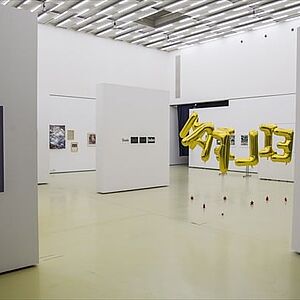 Die Ausstellungsräume und mittig darin gelbe, halbhoch im Raum schwebende, Buchstabenballons