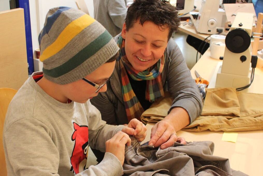 Eine Dame zeigt einem junge Buben im Repair Cafe wie kaputte Dinge wieder funktionieren.