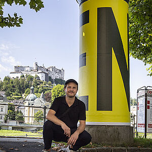 Der Künstler Daniel Car neben seiner Litfaßsäule als Endlos-Schleife rund um die Annoncier-Säule am Giselakai 47. 
