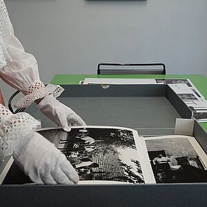 Eine Hand mit Handschuhen hebt eine Fotografie vom Tisch auf.