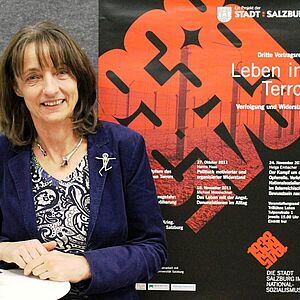 Helga Embacher neben einem Plakat von der Stadt Salzburg