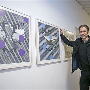 Csaba Fürjesi stütz sich an die Wand zwischen zwei seiner abstrakten Bilder mit weißem Rahmen.