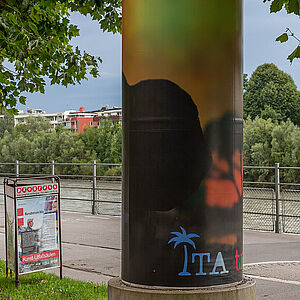 Litfaßsäule mit dem Kunstplakat im Hintergrund der Geh- und Radweg entlang der Salzach und der Fluss