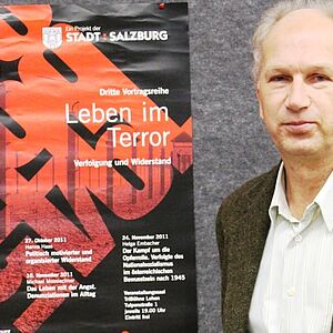 Ein Mann steht rechts neben einem Plakat der Stadt Salzburg