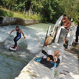 Ein Surfer surft auf der Almwelle und andere Surfer stehen auf der Seite und sehen zu.