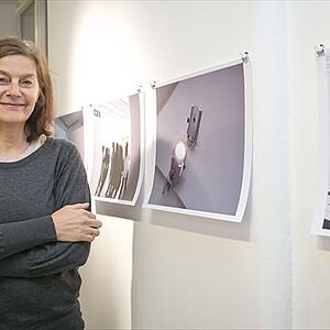 Sigrid Kurz steht neben ihren an der Wand hängen, ungerahmten Fotografien.