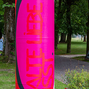 Litfaßsäule mit dem Kunstplakat, im Hintergrund der Volksgartenpark