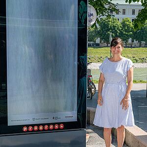 Martina Mühlfellner neben ihrem Werk "take a break-curtain in" auf digitalen city lights im Stadtraum.