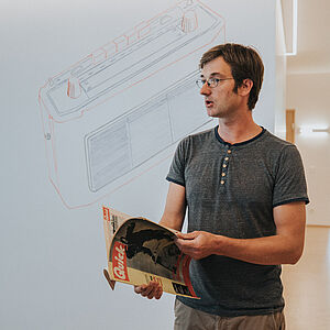 Der Künstler vor der Beamer-Leinwand mit dem Motiv Kofferradio, hält ein Exemplar aus seiner Zeitschriftensammlung in der Hand