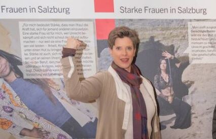 Starke Frauen in Salzburg, Frauenbeauftragte Alexandra Schmidt Eine Frau steht vor einem Plakat um die Staerke der Frauen zu promoten.