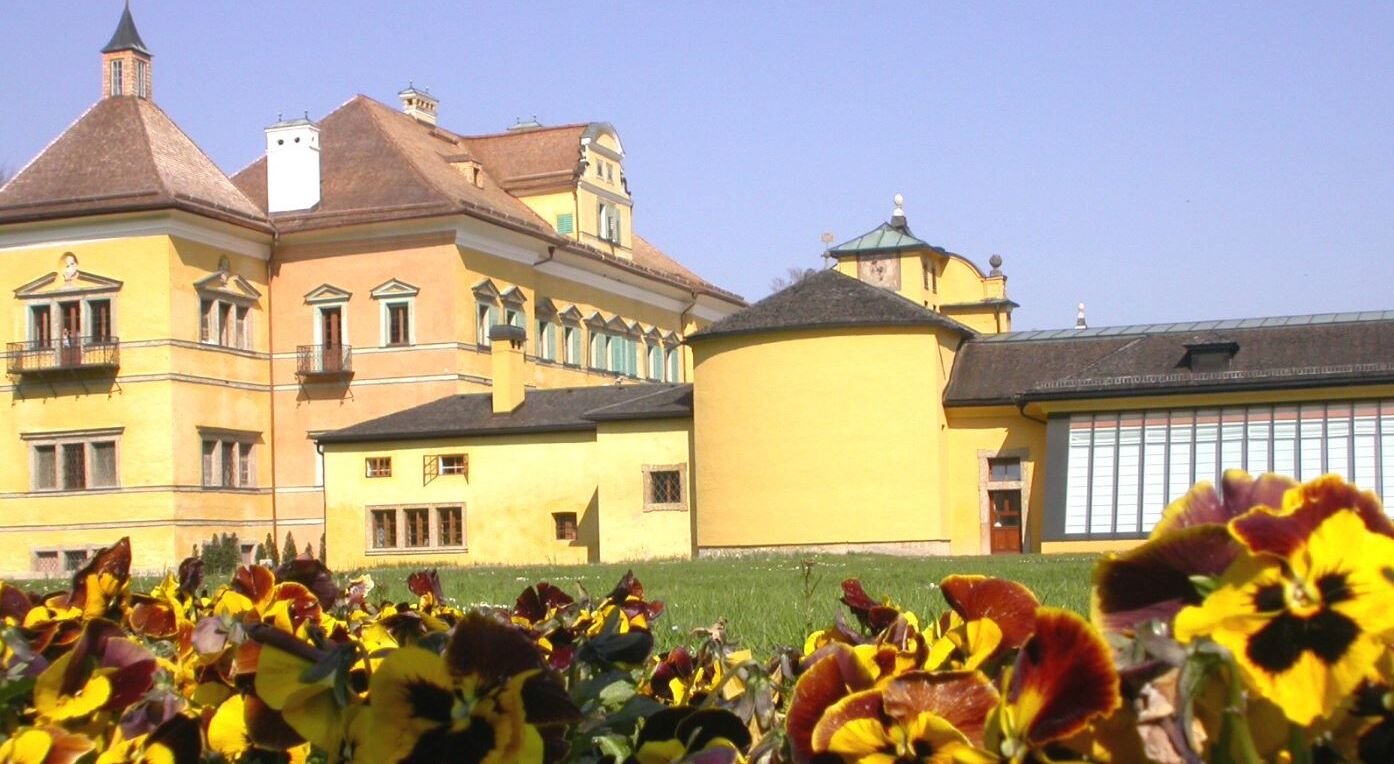 Das Schloss Hellbrunn, fotografiert von außen, vor schönen Blumenbeeten.