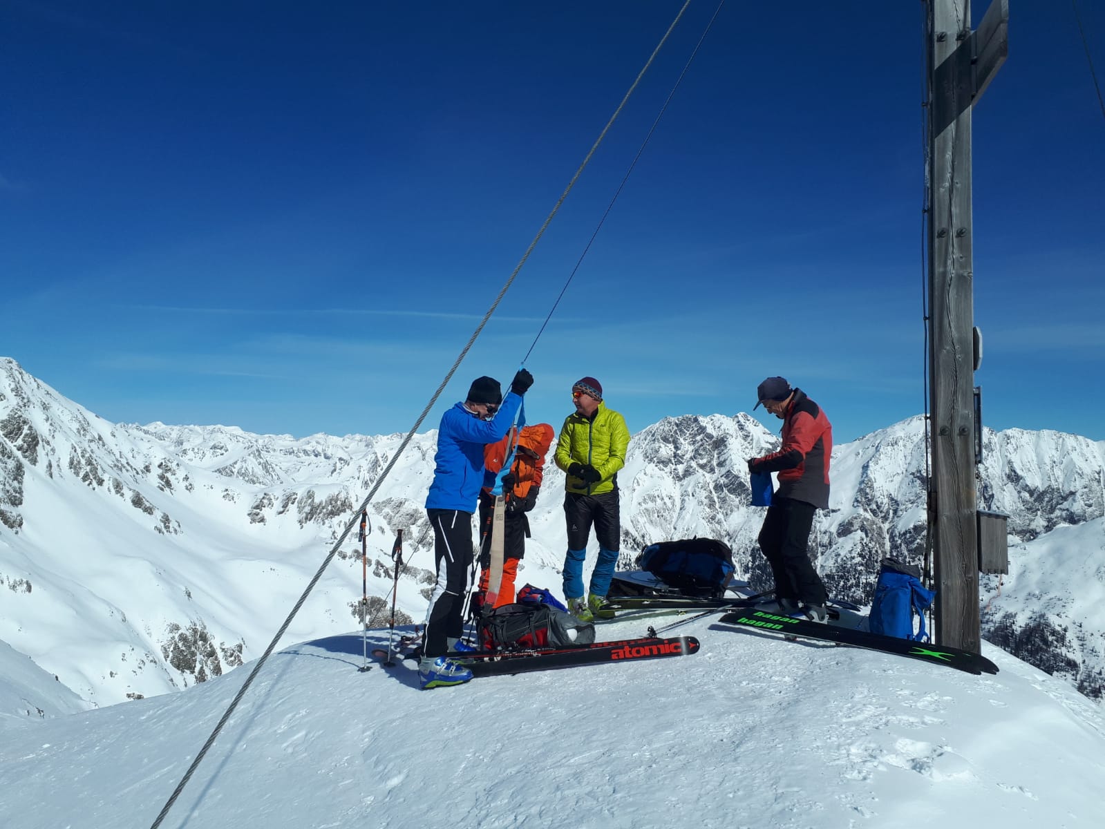 Tourengeher neben dem Gipfelkreuz - Ausblick auf schneebedekte Gebirgszüge