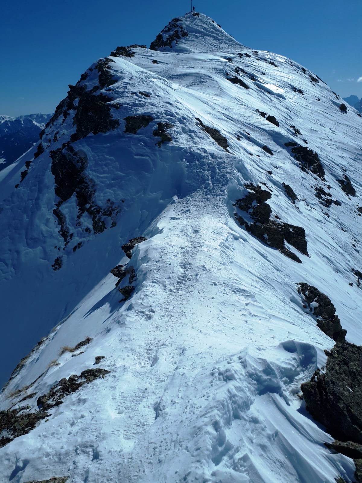 Abstieg entlang des Gipfelgrates auf blank gepresstem Schnee
