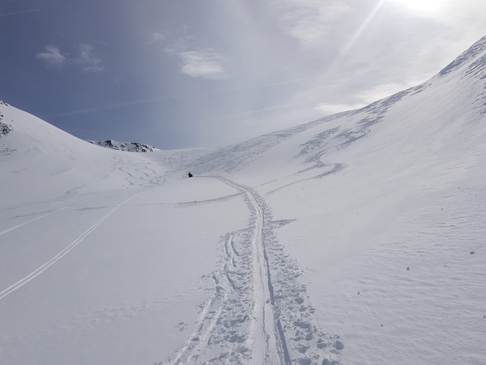 vereinzelte Spuren entlang verschneiter Berghänge, im Hintergrund die Spitze eines Gipfels sichtbar