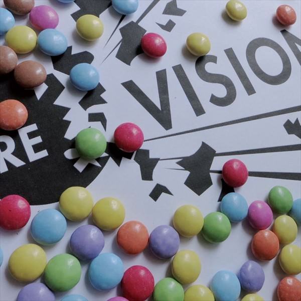 Schriftzug "RE - VISION" in schwarz-weiß und darauf verteilt liegend viele bunte Smarties