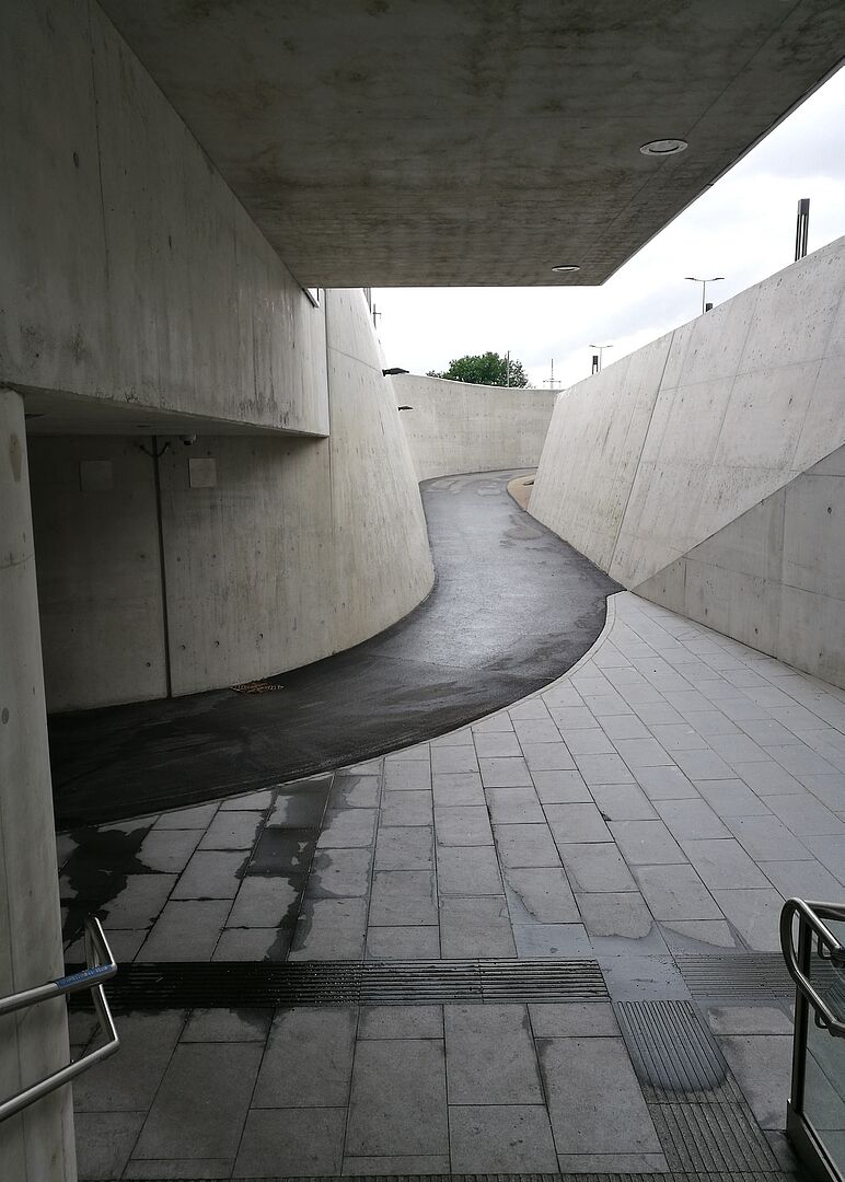 schwaz-weiß Foto einer asphaltierten Straßenabfahrt zwischen Beton-Seitenwänden in eine Unterführung