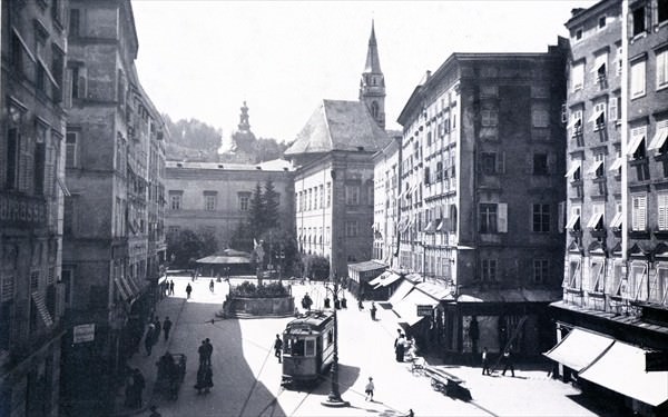 Schwarz-Weiss Fotografie des Alten Marktes mit dem Florianibrunnen zwischen den Häuserreihen und im Vordergrund die Strassenbahn im Jahre 1910.