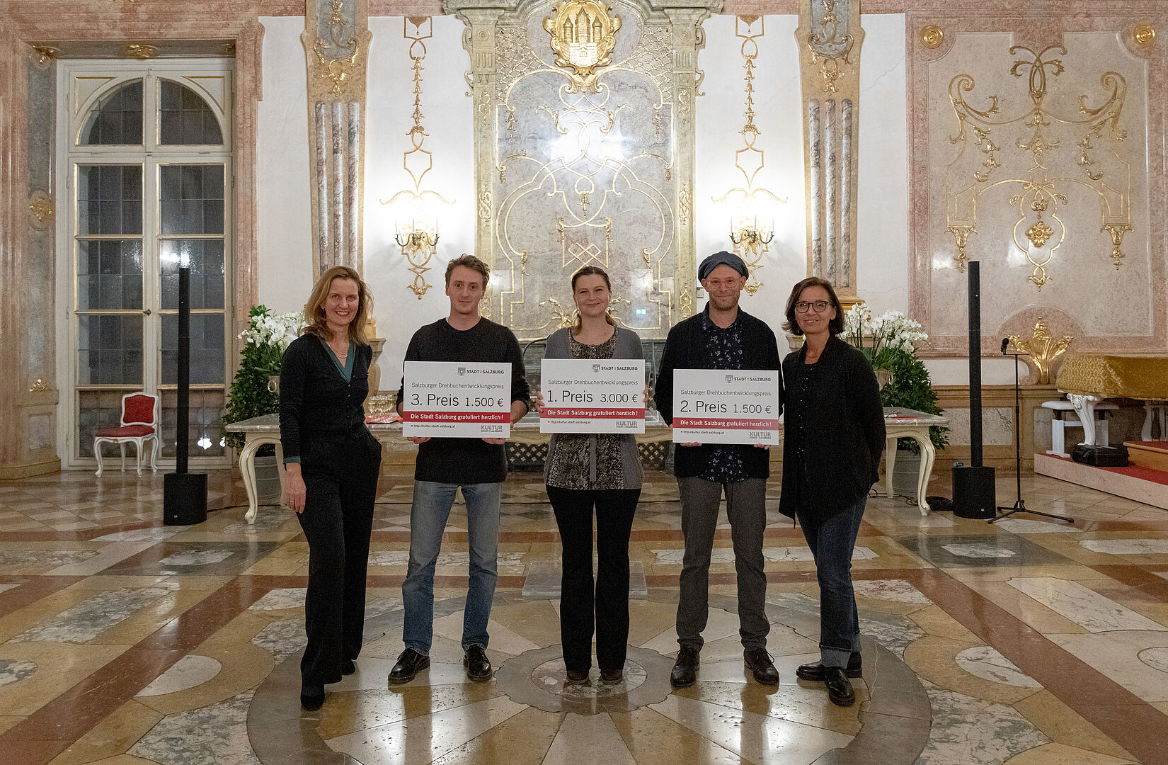 Gruppenfoto im Marmorsaal Schloß Mirabell; die Preisträger halten ihre Preise in Form von übergroßen Gutscheinen vor dem Körper in Händen.