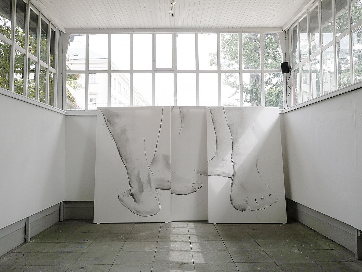 Wo Göttinnen entstehen... Ausstellungsansicht. Drei auf Leinwand gezeichnete, großformatige Skizzen der Fußpartien der Göttinnen lehnen an der Galeriewand. Über den Leinwänden ist das Fensterband der Stadtgalerie Zwergelgarten zu sehen.